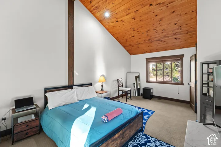 Vaulted wood-paneled ceiling, white walls, exposed wood beam, wood-trimmed window, and neutral carpeting