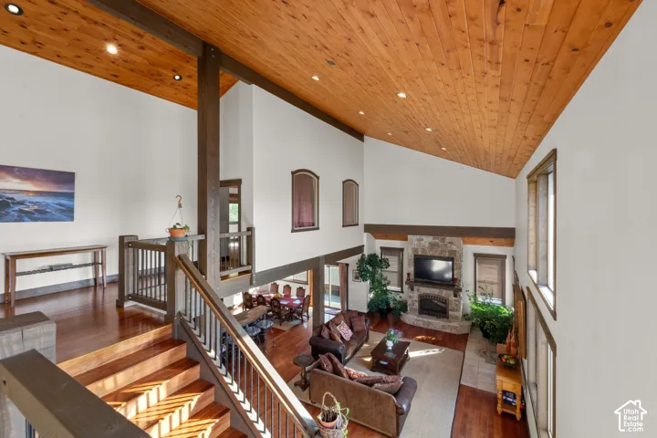 Vaulted wood-paneled ceiling with recessed lighting, wood-finish flooring, stone-clad fireplace with mantel, exposed wood beams, and a wood staircase with railing