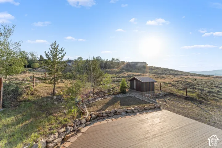 Expansive outdoor decking with a stone retaining wall, bordering a detached storage shed and natural landscaping