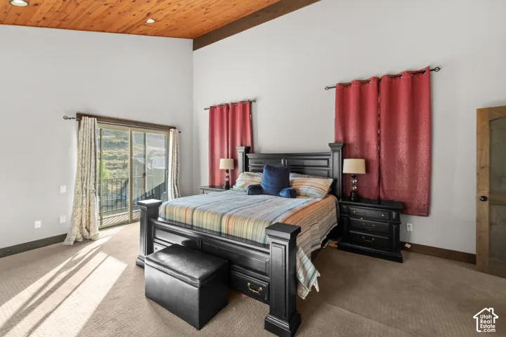 Vaulted wood-paneled ceiling with recessed lighting, carpeted flooring, sliding glass door with balcony access, and a wood-finish door