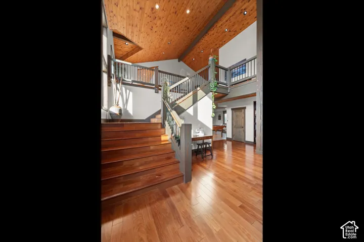 Wood-finish flooring, exposed wood beam ceiling, vaulted ceilings, two-story entryway, and wood staircase with railing