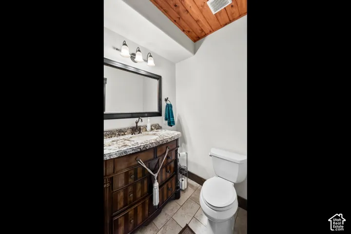Vanity with a decorative wood-finish cabinet, a single basin sink, a stone-finish countertop, and a three-light fixture