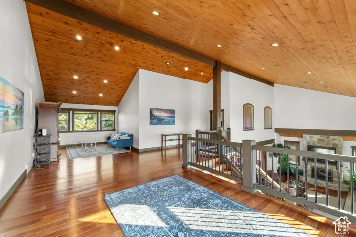 Vaulted wood-paneled ceiling with recessed lighting, wood-finish flooring, interior balcony with wood railing, white walls, and built-in stone fireplace below