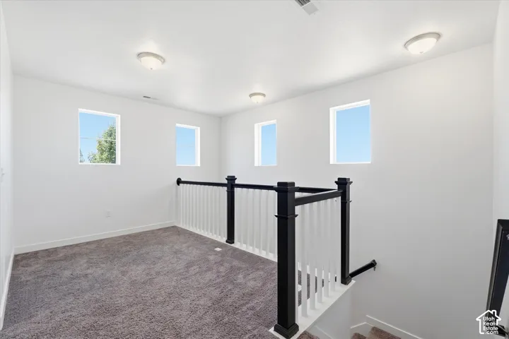 Carpeted landing with a white and black staircase railing, four distinct windows, and ceiling-mounted light fixtures