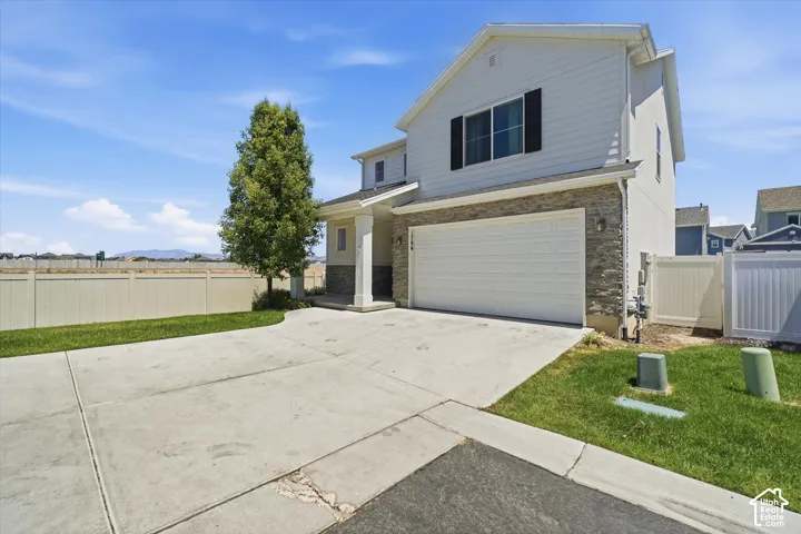 Exterior featuring light-colored siding, stone facade accents, an attached garage, a paved driveway, and a fenced yard