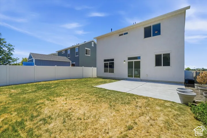 White stucco exterior, sliding glass door, multiple windows, concrete patio, and a white privacy fence