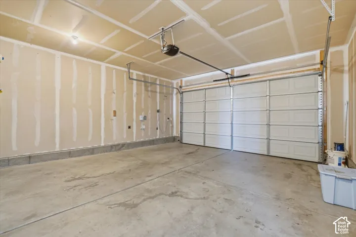 Spacious garage with an automatic overhead door, concrete flooring, and exposed ceiling joists