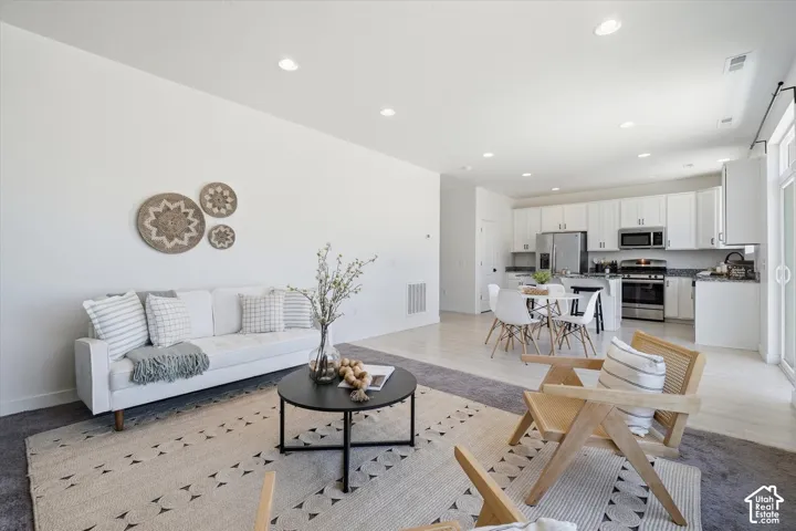 Open-concept living space featuring recessed lighting, light wood-finish flooring, white cabinetry, and stainless steel appliances
