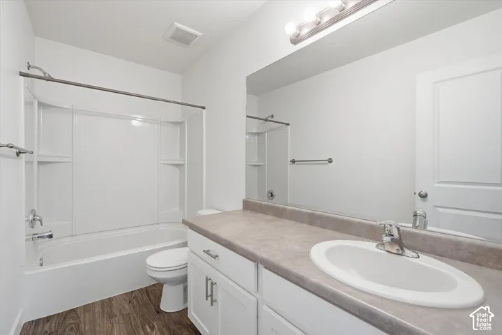 Bathroom featuring a white vanity with an integrated sink, a large wall-mounted mirror, a bathtub with a shower, and wood-finish flooring