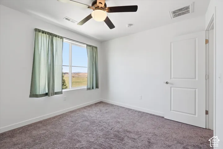 Expansive window with natural scenery, ceiling fan with integrated lighting, paneled interior door, and plush carpet flooring