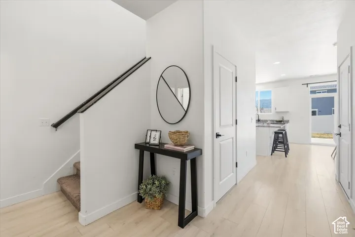 Light wood-finish flooring extending through the entry, white interior doors with matte black hardware, and a staircase featuring a black handrail and carpeted treads
