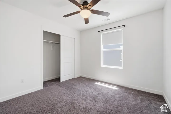 Recessed window with roller shade, dark gray carpeting, ceiling fan with integrated lighting, built-in closet with sliding panel doors