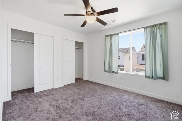 Neutral wall paint, ceiling-mounted fan with integrated lighting, two sliding closet doors, and broad window with drapery