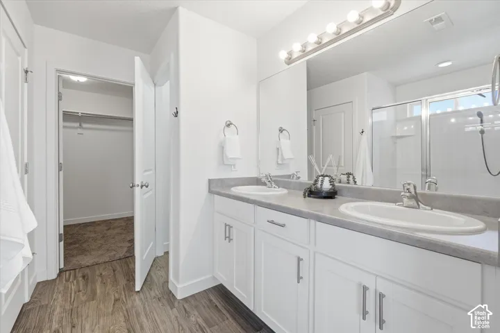Double vanity with integrated sinks, wood-finish flooring, white cabinetry with brushed nickel hardware, and a glass-enclosed shower with a window