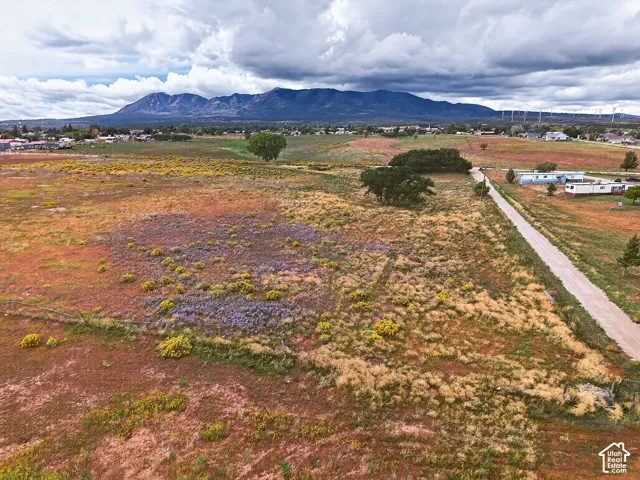 Expansive rural landscape featuring a dirt road, scattered trees, and distant mountains