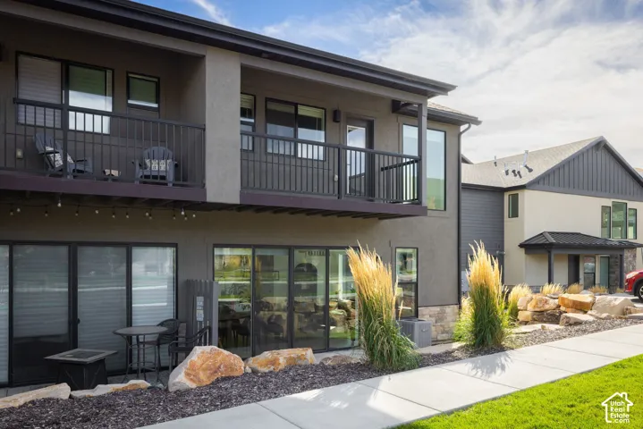 Exterior featuring a stucco finish, stone accents, multiple balconies with metal railings, and ground-level patios with sliding glass doors