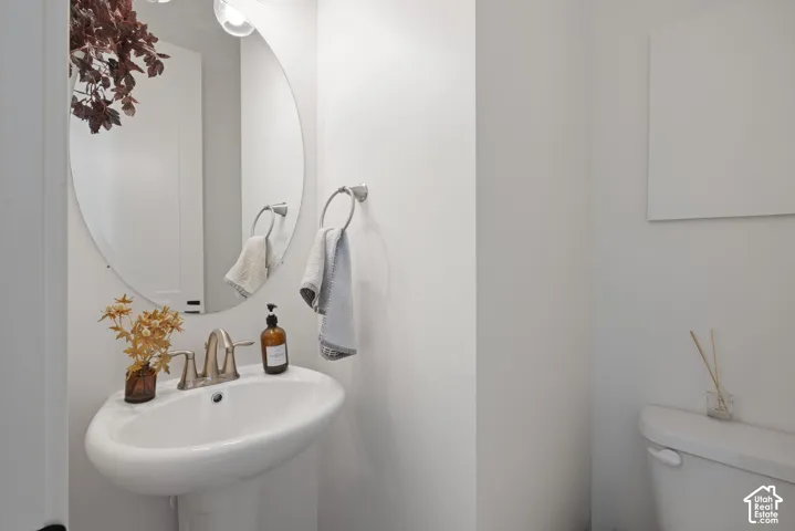 Pedestal sink with brushed nickel faucet, oval mirror, and wall-mounted light fixture