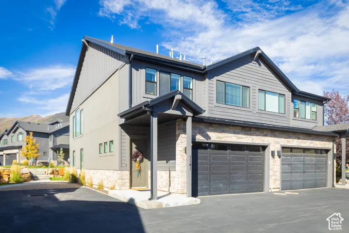 Contemporary residence featuring a covered entry, stone facade accents, two garage doors, and dark gray siding