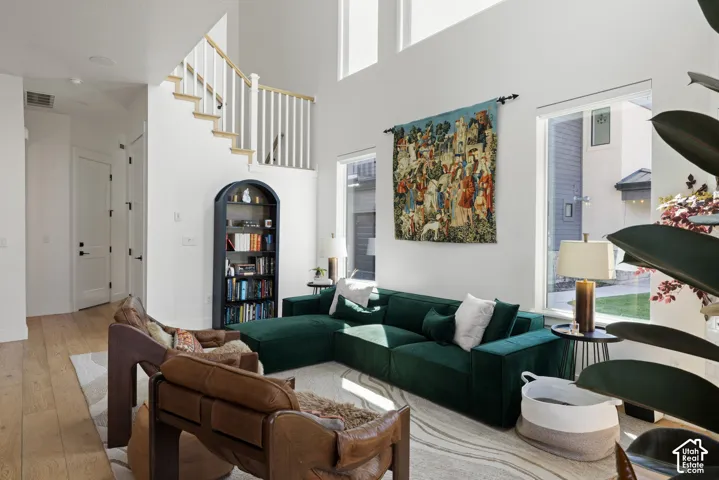 Two-story ceiling, large windows, wood-finish flooring, staircase with white balusters, and a built-in arched display cabinet