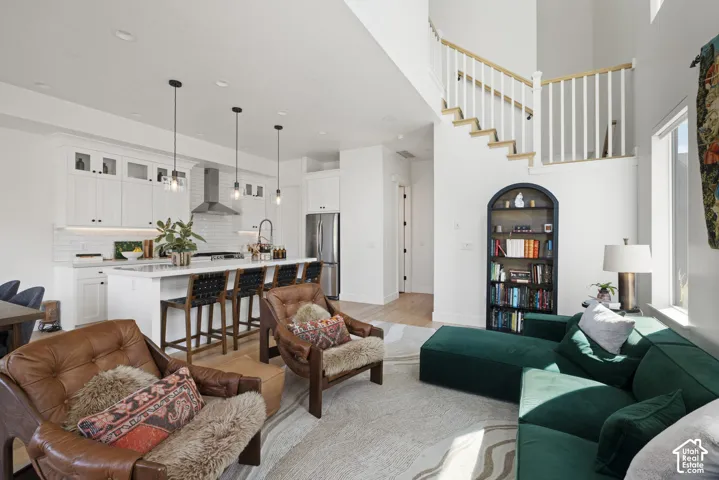 Open-concept living area featuring a kitchen island with seating, white shaker cabinetry, stainless steel appliances, and a dual-height staircase with wood treads and white balusters