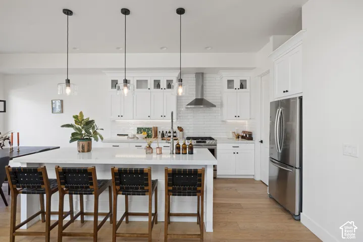 Kitchen featuring a large island with seating, white shaker cabinetry, stainless steel appliances, and wood-finish flooring