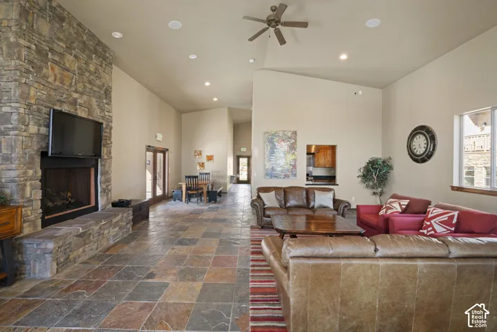 Vaulted ceilings, recessed lighting, ceiling fan, stone-clad fireplace with hearth, and multi-tone tile flooring