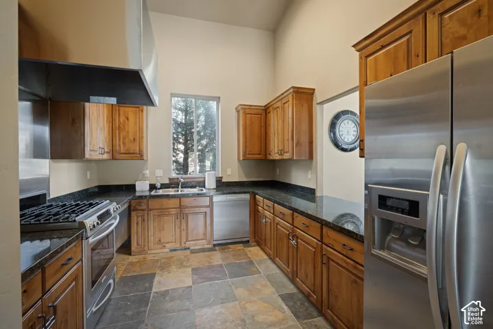 Kitchen featuring stainless steel appliances, wood cabinetry, dark countertops, and varied-tone flooring