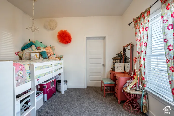 Bright bedroom retreat featuring carpet flooring, white six-panel closet door, pendant lighting fixture, and floral window treatments with coordinating hardware
