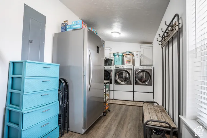 Dedicated laundry room featuring side-by-side washer and dryer units, stainless steel refrigerator, wood-finish flooring, bright overhead lighting, and ample storage with turquoise cabinetry and open shelving for household supplies and equipment