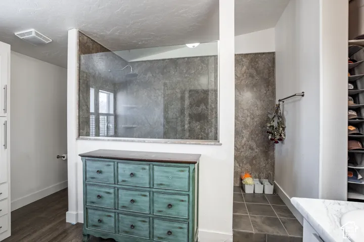 Spa-inspired primary bathroom featuring a frameless glass shower enclosure with stone-look tile surround, floating vanity with turquoise painted cabinetry and nine drawers, white quartz countertop, dark wood-finish flooring, and a soaking tub positioned n