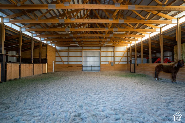 Spacious equestrian arena featuring a wood beam ceiling, corrugated metal walls, and dedicated stalls