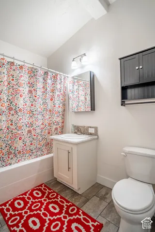 Bright, updated bathroom featuring a ceramic pedestal sink with chrome fixtures, white subway tile surround with colorful patterned shower curtain, tile flooring, wall-mounted cabinetry with ample storage, and a one-piece toilet with elongated bowl