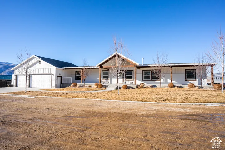 White exterior siding, dark-framed windows, prominent two-car garage, covered entry porch, and mature landscaping