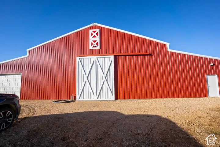 Striking red metal barn featuring a peaked roof with cupola detail, large white X-pattern sliding doors, and corrugated steel siding