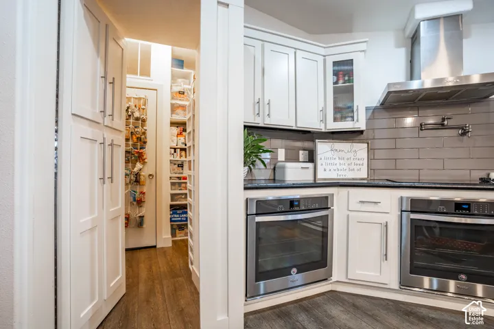 Contemporary kitchen featuring white cabinetry with glass-front upper cabinets, stainless steel dual wall ovens, subway tile backsplash, and wood-finish flooring