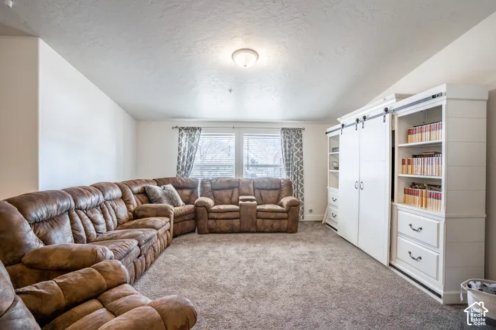 Spacious recreation room featuring a sectional leather conversation area, neutral carpet flooring, large windows with custom drapery, and built-in white cabinetry with shelving