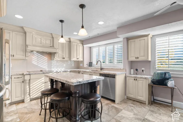 Kitchen with light-toned cabinetry, a central island with countertop seating, stainless steel appliances, and a tiled backsplash