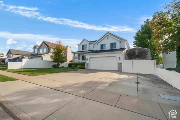 Two-story exterior with white siding and stone accents, attached garage, extended driveway, and white privacy fencing