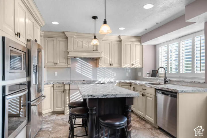 Kitchen featuring light-toned cabinetry, stainless steel appliances, a center island with seating, stone countertops, and a tile backsplash