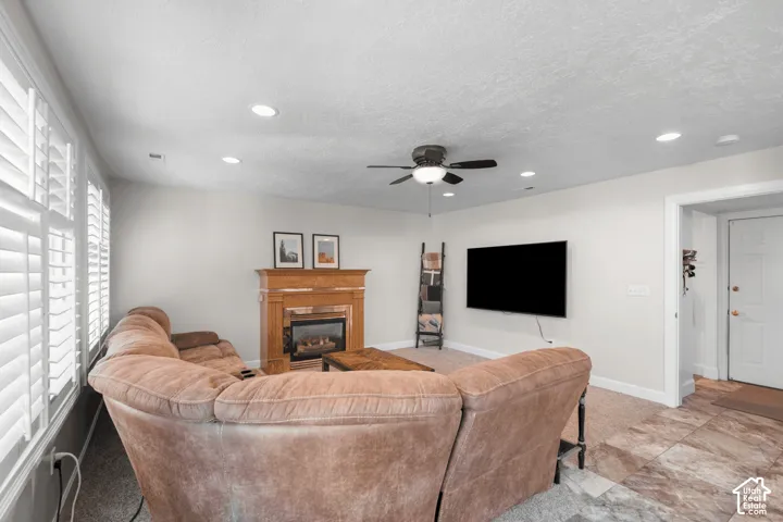 Recessed lighting, wood-finish fireplace mantel with stone surround, ceiling fan, plantation shutters, and large-format tile flooring