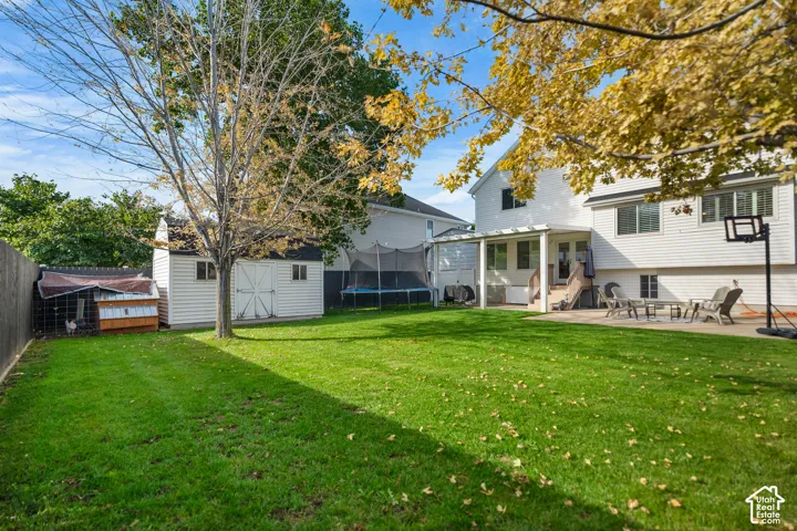 Expansive backyard featuring a lush lawn, white siding, a covered patio, and a storage shed