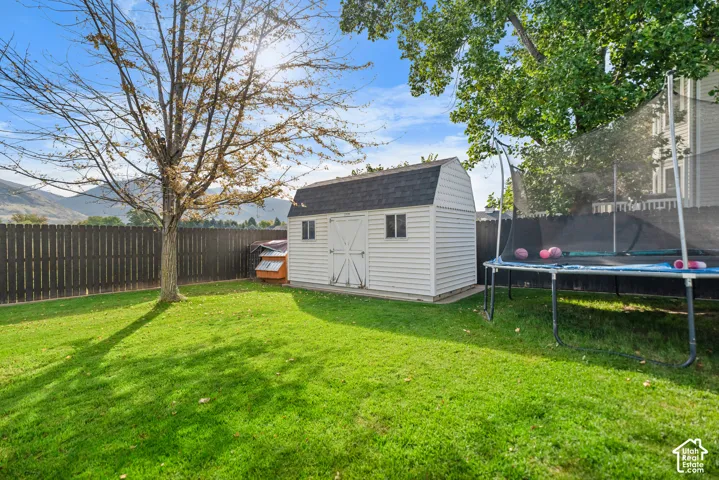 Expansive backyard featuring a manicured lawn, established shade trees, a picket fence, and a storage shed with a gambrel roof