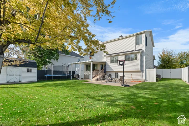 Expansive backyard featuring a manicured lawn, a detached storage shed, a white privacy fence, and a concrete patio