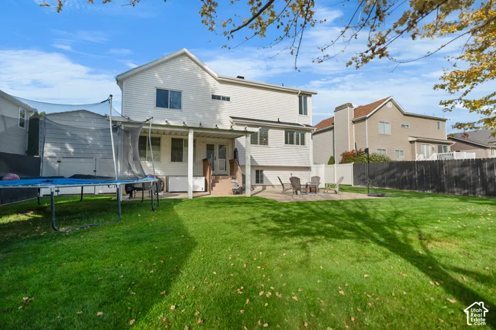 Expansive backyard with a manicured lawn, paved patio, covered porch, and mature perimeter fencing