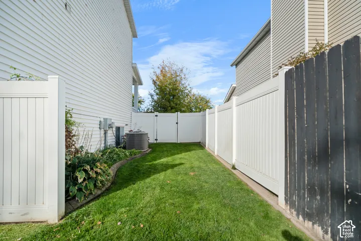 Enclosed yard featuring a manicured lawn, white privacy fencing, and a landscaping bed with mature plantings