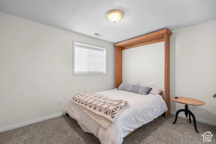 Built-in wooden bed frame, window with blinds, overhead flush mount lighting, and gray carpet flooring