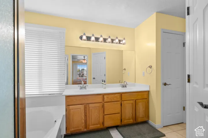 Dual sink vanity with wood-finish cabinetry, a large wall-mounted mirror, and an integrated bathtub with a window