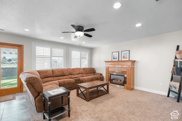Recessed ceiling lighting, a ceiling fan, wood-frame glass panel door, plantation shutters, and a wood-mantel fireplace with electric insert