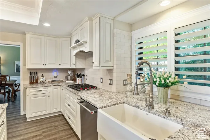 White shaker-style cabinetry with dark hardware, granite countertops, a white subway tile backsplash, stainless steel appliances, and wood-finish flooring