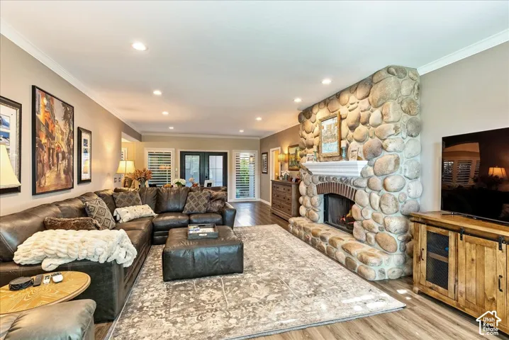 Expansive living area featuring a stone fireplace with a brick arch and mantle, wood-finish flooring, recessed lighting, and crown molding